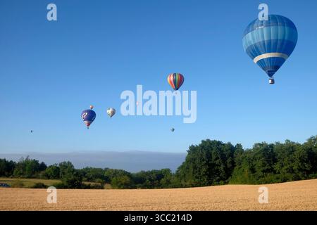 Eine Reihe von acht Heißluftballons, die über die französische Landschaft treiben Stockfoto