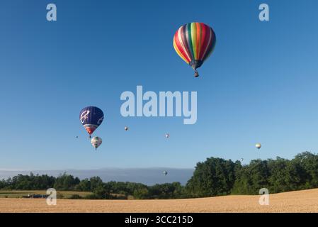 Eine Reihe von neun Heißluftballons, die über die französische Landschaft treiben Stockfoto