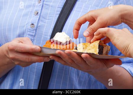 Person, die Freunden traditionelle Desserts anbietet, wobei das Teilen und die Verbindung über gutes Essen in einem Marktumfeld hervorgehoben wird. Stockfoto