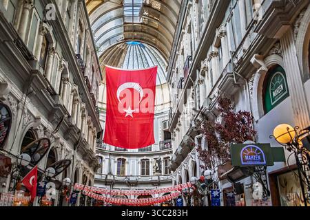Istanbul, Türkei - 11. November 2023: Verziertes Inneres des historischen, von Cicek Pasaji überdachten Passageways, eine große türkische Flagge, die vom Glasdach hängt Stockfoto