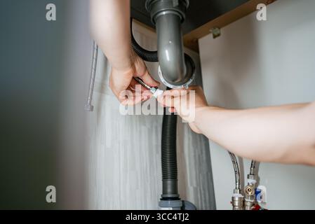Professionelle Klempner arbeiten unter dem Küchenspüle, verbinden die Wasserleitung mit dem Mischer und führen Wartungs- und Reparaturarbeiten mit Präzision und Fachkenntnis durch Stockfoto