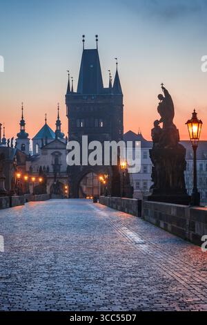Karlsbrücke in Prag, Tschechische Republik, bei Sonnenaufgang mit leuchtenden Straßenlaternen, historischen Türmen und Silhouetten barocker Architektur Stockfoto