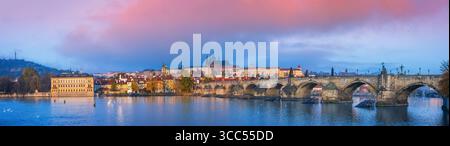 Panoramablick auf Prag mit Karlsbrücke, Moldau und Prager Burg bei Sonnenaufgang, farbenfrohen Wolken und historischer Architektur, die sich auf dem widerspiegelt Stockfoto