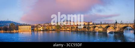 Panoramablick auf Prag mit Karlsbrücke, Moldau und Prager Burg bei Sonnenaufgang, farbenfrohen Wolken und historischer Architektur, die sich auf dem widerspiegelt Stockfoto