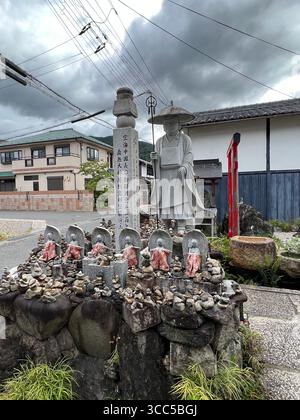 Buddhistische Statuen und eine gekleidete Mönchsstatue mit Steinopfern an einem ruhigen Schrein in Kyoto, Japan. Stockfoto