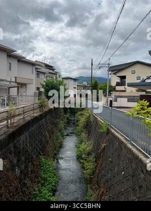 Ein rotes Torii-Tor führt zu einem kleinen Schrein-Innenhof in Kyoto, Japan, umgeben von Steinlaternen und Opfersteinen. Stockfoto