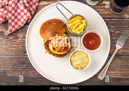 Köstlicher Gourmet-Burger mit Cheddar-Käse, gebratenen Zwiebeln, Krautsalat und Pommes frites Stockfoto
