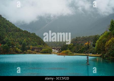 Der türkisfarbene See reflektiert nebelbedeckte Berge und üppige Wälder im Blue Moon Valley, Lijiang, China. Stockfoto