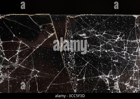 Zerbrochen mit vielen Schäden und Glasstücken auf schwarzem Hintergrund, dünnes Glas in viele Stücke gebrochen, Nahaufnahme Stockfoto