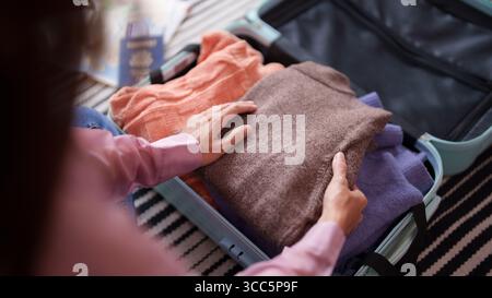 Hände für Erwachsene ordnen Sie die gefalteten Kleidungsstücke sorgfältig in einem offenen Koffer an. Für die Abfahrt ist ein Reisepass sichtbar. Stockfoto