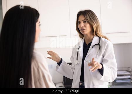 Ernsthafte Ärztin im Laborkittel, die mit einer Patientin spricht Stockfoto