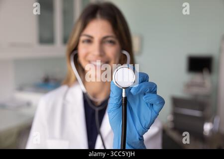 Positive junge Herzärztin zeigt Stethoskopsensor vor der Kamera Stockfoto