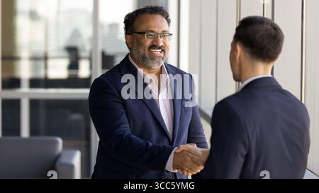 Fröhlicher, älterer Geschäftsinhaber, der sich mit jüngeren Beratern die Hand schüttelt Stockfoto