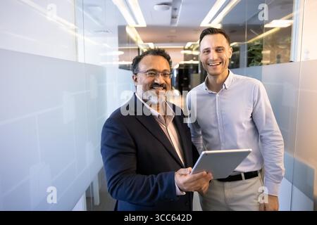 Glückliche, vielseitige ältere und jüngere männliche Geschäftspartner stehen zusammen Stockfoto