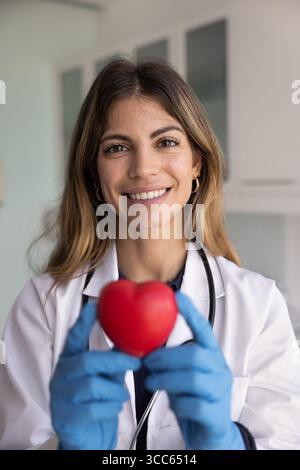 Glückliche junge Herzchirurgin, die ein rotes Spielzeugherz hält Stockfoto
