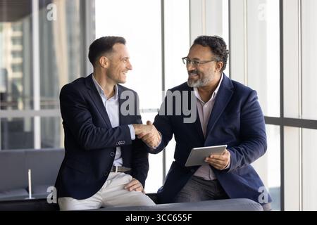 Glückliche multiethnische jüngere und ältere Geschäftspartner schütteln die Hand Stockfoto