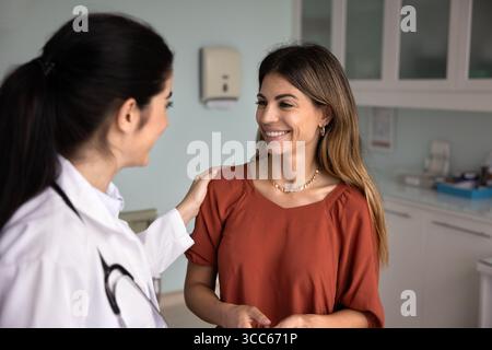 Junge optimistische Hausärztin, die die Schulter eines lateinischen Patienten berührt Stockfoto