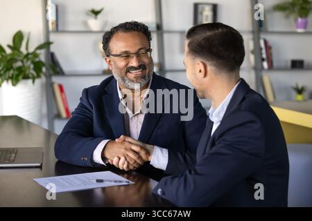 Glücklicher, älterer indischer Geschäftsmann, der sich mit jüngeren Geschäftspartnern die Hand schüttelt Stockfoto
