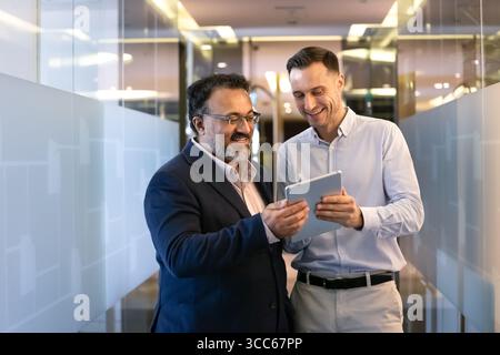 Positive multiethnische jüngere und ältere Geschäftskollegen verwenden ein digitales Tablet Stockfoto