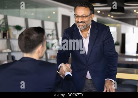 Glücklicher, älterer indischer Geschäftsmann, der sich mit jüngeren Geschäftspartnern die Hand schüttelt Stockfoto