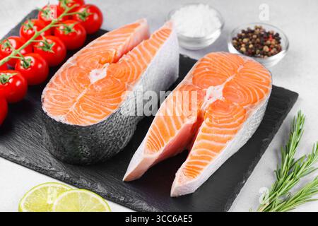 Zwei frische, rohe Lachs- oder Forellensteaks auf weißer Steinoberfläche mit Lebensmittelzutaten. Tomaten, Limette, Rosmarin, Salz und Pfeffer. Gesunde Ernährung, Meeresfrüchte Stockfoto