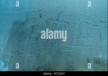 Auf kaltem Glas bildet sich Kondenswasser, Tropfen laufen aus Glas. Feuchte Innenatmosphäre. Schuss von Tropfen auf nassem Fenster. Nebelfenster mit starker Feuchtigkeit (Fortsetzung Stockfoto