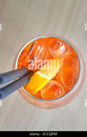 Aperol Spritz Cocktail aus nächster Nähe mit einer Zange, die Eiswürfel in einem Glas hält Stockfoto