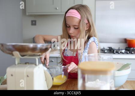 Mädchen, das Eier zum Backen von Kuchen in der Küchenschüssel mit dem Handrührer verquirlt Stockfoto