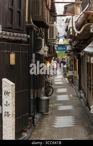 Eine enge Gasse in Japan mit traditioneller Architektur und Gruppen von Menschen. Die Szene zeigt eine authentische urbane Umgebung mit lebhaften Elemen Stockfoto