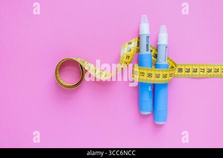 Diabetesmedikation Und Gewichtsverlust Messgeräte Auf Rosa Hintergrund, Mit Insulininjektionsstiften Und Gelbem Maßband. Arzneimittelinjektion Oz Stockfoto