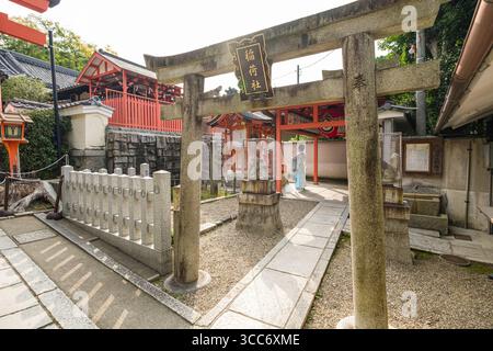 Ruhige Aussicht auf einen traditionellen japanischen Schrein mit einem Torii-Tor aus Stein, umgeben von lebendiger roter Architektur und Grün, mit Entdeckungsreisen Stockfoto