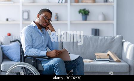 Schwarzer Mann im Rollstuhl, der Notizbuch liest, studiert oder arbeitet von zu Hause aus Stockfoto