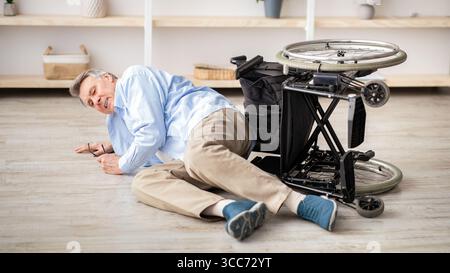 Älterer Mann mit körperlicher Behinderung, der nach einem Sturz auf dem Boden liegt Unten von seinem Rollstuhl zu Hause Stockfoto