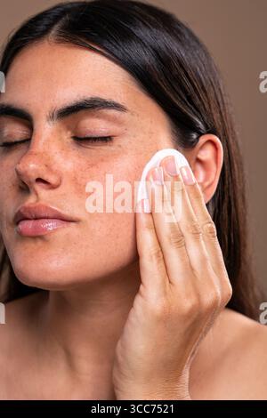 Beauty-Porträt mit einer jungen Frau, die ihr Gesicht sanft mit einem Wattepad reinigt und dabei Hautpflegeroutinen, Kosmetik und die Verfolgung einer Ra hervorhebt Stockfoto