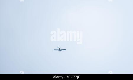 Minimalistisches Bild eines kleinen einmotorigen Flugzeugs von hinten, das durch einen klaren blauen Himmel fliegt. Ideal für Reisen, Luftfahrt und Transport Stockfoto