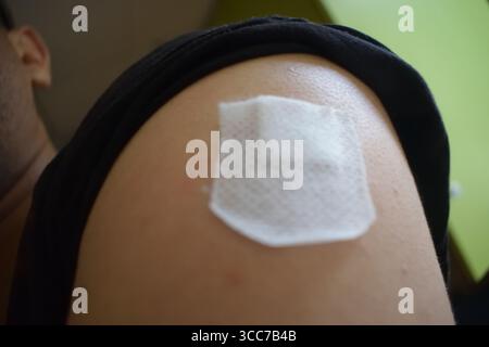 Nicht bearbeitetes Foto Nahaufnahme des Oberarms einer Person, das ein weißes medizinisches Pflaster oder Verband auf die Haut aufträgt. Das Foto hebt Details hervor Stockfoto