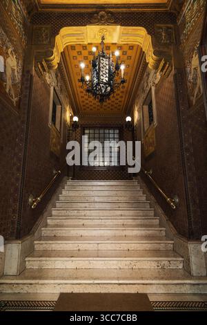 Elegante Marmortreppe in einem historischen römischen Gebäude (Viertel Coppedè) mit kunstvollen Kronleuchtern – klassische europäische Architektur vom Feinsten Stockfoto