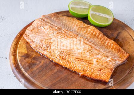 Würzige Zitrushälften ergänzen das gebackene Lachsfilet auf einem warmen Holzbrett Stockfoto