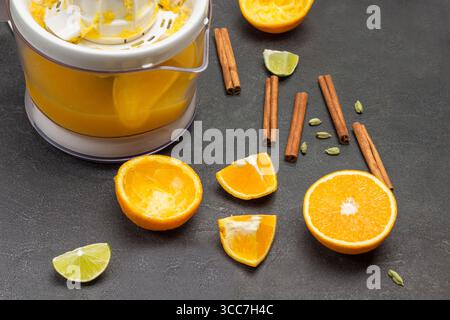 Orangenhälften und Gewürze auf dem Tisch. Entsafter mit Fertigsaft. Schwarzer Hintergrund. Draufsicht Stockfoto
