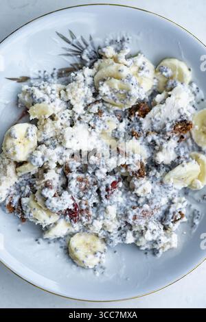 Nahaufnahme von Hüttenkäse mit Banane, Müsli und Chiasamen auf einem Teller. Stockfoto