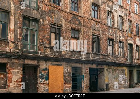 Verlassenes Backsteingebäude, städtisches Verfallsrenovierungskonzept. Verwitterte Fassade mit verdeckten Fenstern und abblätternder Farbe symbolisiert Vernachlässigung, Armut und Pote Stockfoto