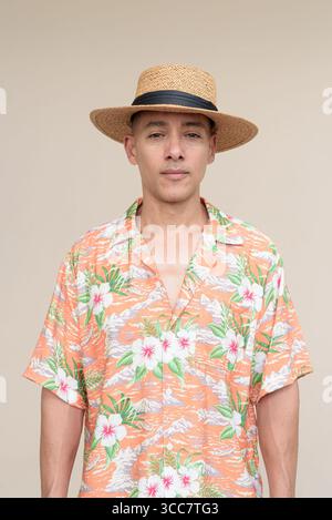 Glücklicher hispanischer Mann mit Panamahut und tropischem hawaiianischem Hemd, gekleidet in legere Sommermode. Der fröhliche Tourist posiert in entspanntem Urlaub Stockfoto
