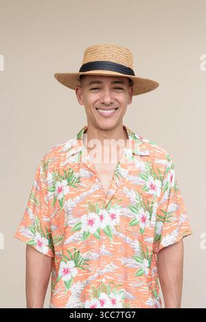 Glücklicher hispanischer Mann mit Panamahut und tropischem hawaiianischem Hemd, gekleidet in legere Sommermode. Der fröhliche Tourist posiert in entspanntem Urlaub Stockfoto