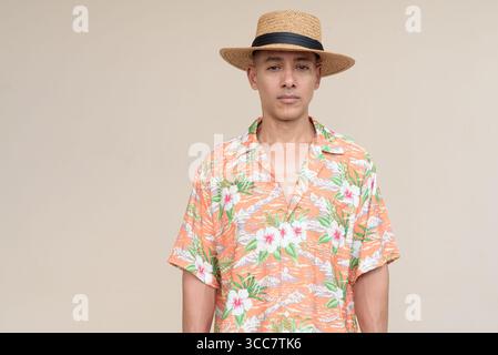 Glücklicher hispanischer Mann mit Panamahut und tropischem hawaiianischem Hemd, gekleidet in legere Sommermode. Der fröhliche Tourist posiert in entspanntem Urlaub Stockfoto