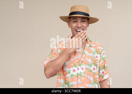 Glücklicher hispanischer Mann mit Panamahut und tropischem hawaiianischem Hemd, gekleidet in legere Sommermode. Der fröhliche Tourist posiert in entspanntem Urlaub Stockfoto