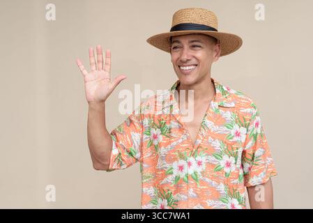 Glücklicher hispanischer Mann mit Panamahut und tropischem hawaiianischem Hemd, gekleidet in legere Sommermode. Der fröhliche Tourist posiert in entspanntem Urlaub Stockfoto