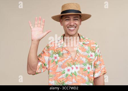 Glücklicher hispanischer Mann mit Panamahut und tropischem hawaiianischem Hemd, gekleidet in legere Sommermode. Der fröhliche Tourist posiert in entspanntem Urlaub Stockfoto