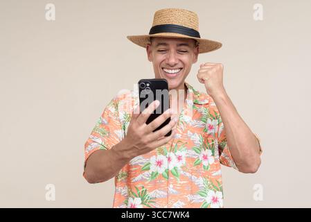 Glücklicher hispanischer Mann mit Panamahut und tropischem hawaiianischem Hemd, gekleidet in legere Sommermode. Der fröhliche Tourist posiert in entspanntem Urlaub Stockfoto