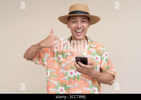 Glücklicher hispanischer Mann mit Panamahut und tropischem hawaiianischem Hemd, gekleidet in legere Sommermode. Der fröhliche Tourist posiert in entspanntem Urlaub Stockfoto