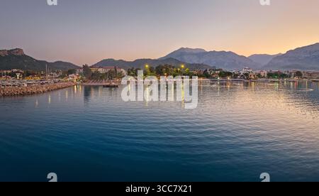 Abenddämmerungsszene in Kemer, Türkei, zeigt die beleuchtete Küste und den Strand der Stadt, die sich wunderschön auf dem ruhigen Meer spiegeln. Majestätische Stier Berge Silhou Stockfoto